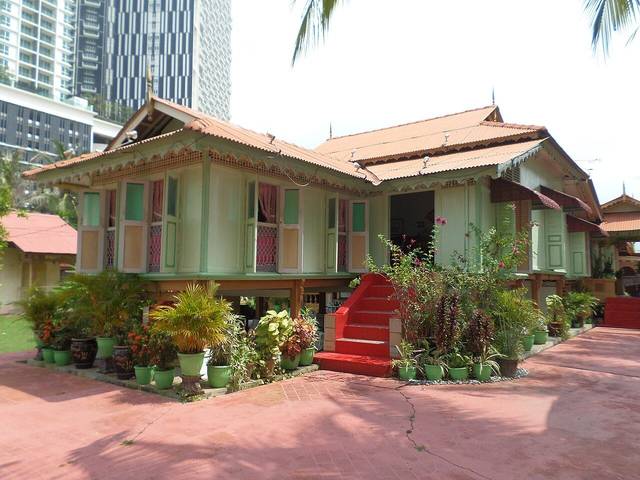 Villa Sentosa, a green and cream traditional Malay house on stilts in Kampung Morten with potted plants in front