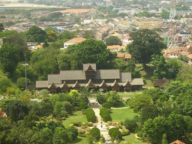 The dark timber roofs of the Melaka Sultanate Palace Museum seen from above, surrounded by gardens