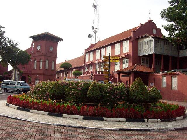 The red Stadthuys building and clock tower in Dutch Square, Melaka, with a flower bed in front