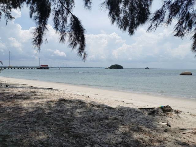 White sand and shallow water on Pulau Besar, with a jetty and a small rocky islet offshore