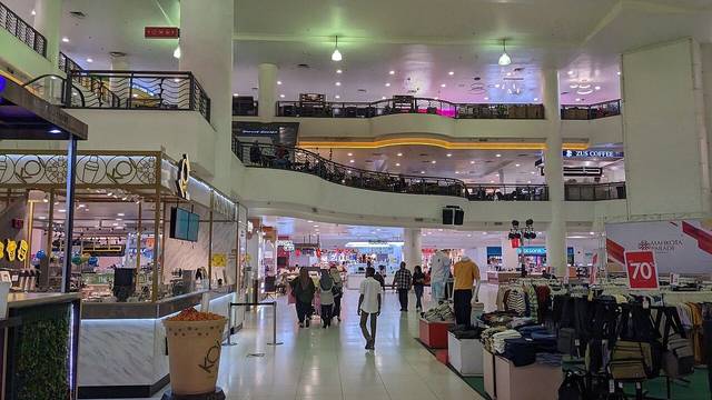 The two-level main hall inside Mahkota Parade shopping centre, with shops, a drinks kiosk and shoppers walking through
