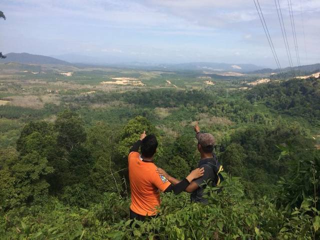 Two hikers pointing out over forested hills and plantations from a viewpoint at Bukit Batu Lebah