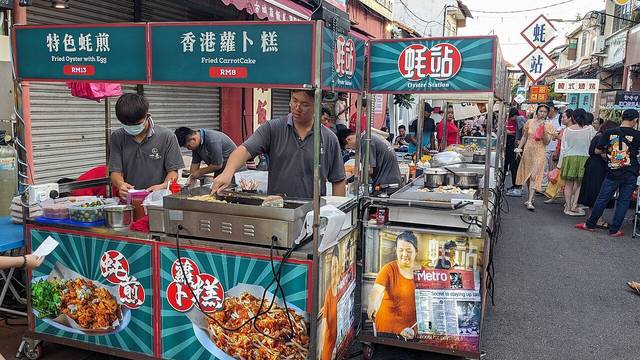 Fried oyster and fried carrot cake stalls with price boards at the Jonker Walk night market in Melaka, photographed in May 2024