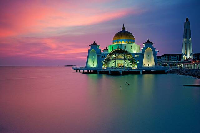 The Melaka Straits Mosque lit up at dusk under a pink sky, reflected in the calm sea