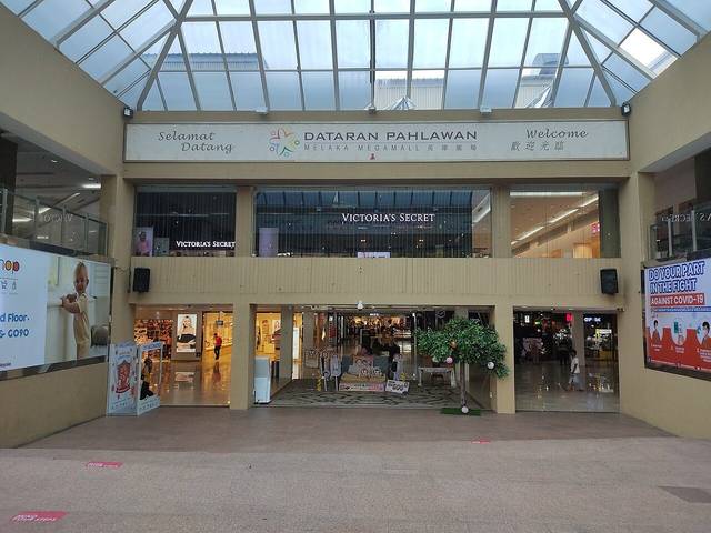 An entrance to Dataran Pahlawan Melaka Megamall under a glass roof, with the bilingual welcome sign above the shopfronts
