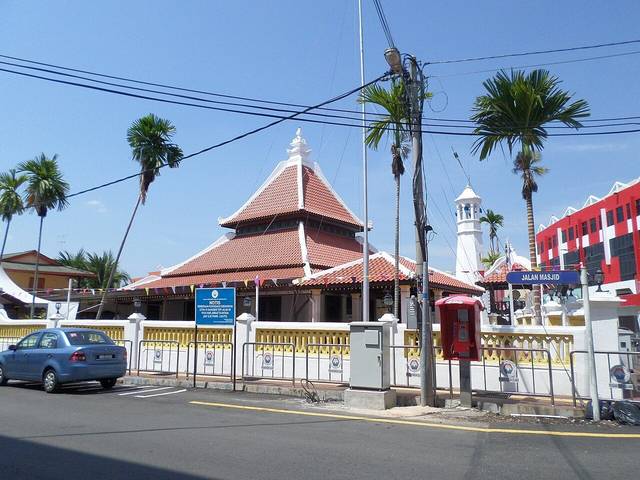 Kampung Hulu Mosque in Melaka with its tiered red-tiled pyramid roof and a slim minaret behind a fence