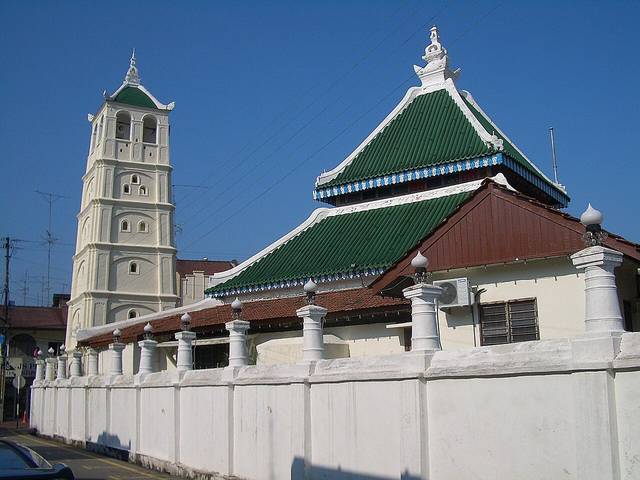 Kampung Kling Mosque with its pagoda-like white minaret and green tiered roof behind a white wall