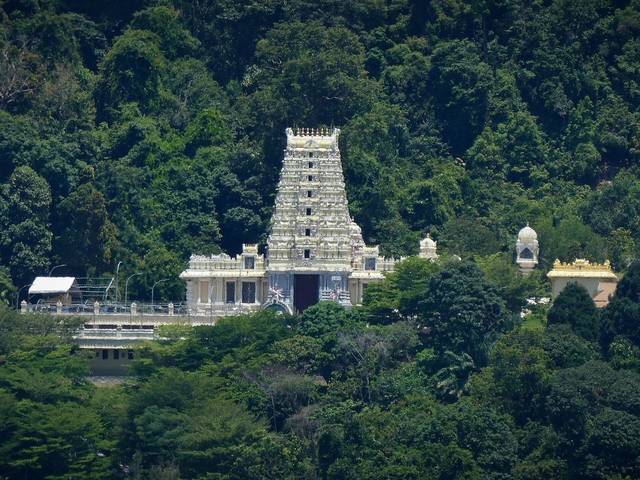 White gopuram of the Waterfall Hilltop Temple set against forested hills, Penang