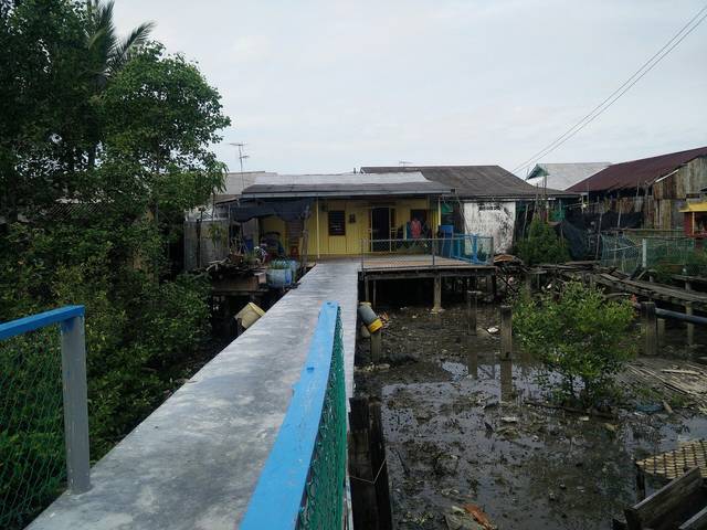 Concrete walkway with a blue rail leading to a wooden stilt house over the mud at Pulau Ketam, Selangor